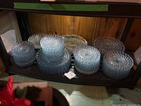Shelf showing multiple stacks of clear and blue glass plates and saucers with a bubble texture pattern.