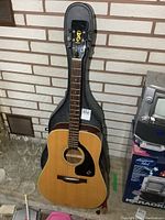 Full front view of guitar in open hardshell case against brick wall