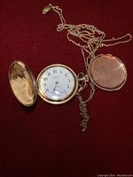 Front of open pocket watch showing white enamel dial with black Arabic numerals and subsidiary seconds; chain looped through crown