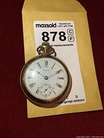 Front view of Waltham gold tone pocket watch showing white dial with Roman numerals, blue hands, and small seconds subdial.