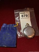 Pocket watch in plastic evidence bag with seller tag and blue velvet pouch.