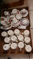 Overview photo showing multiple Royal Albert teacups, saucers, and mugs arranged in cardboard box.