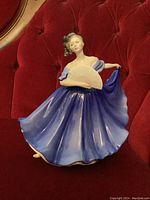 Front view of the Royal Doulton figurine of a lady in a flowing blue dress with fan, showing facial features, dress details, and pose.