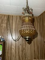 Full view of vintage amber glass swag light fixture hanging on a chain against wood paneling background.