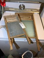 Two vintage wooden washboards placed on top of a washing machine; one smaller Baby Globe branded, one larger Economy Washboard Company branded.
