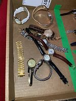 Overview of nine wrist watches and one loose band on cardboard