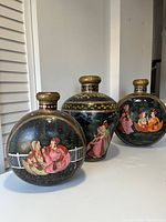 Photo showing three handpainted metal vases with colorful traditional scenes and decorative gold patterns, positioned against a white background.