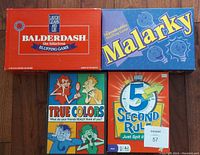 Photo shows four party board games: Balderdash (orange box), Malarky (blue box), True Colors (box with four colored faces), and 5 Second Rule (orange and blue box).