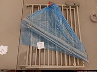 Photo of the adjustable baby gate with vertical bars, beige finish and wrapped blue plastic parts.