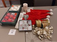 Photo showing two boxes of Christmas ball ornaments (white and red), a set of four red Santa hats, gold-tone bell garland, decorative candle, and a heart-shaped hanging ornament.