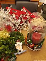 Photo showing the pillar candle holder with red candle inside textured glass and Santa sleigh decorative base, the wooden snowman decoration, plug extender, and white string outdoor lights tangled around a red box.