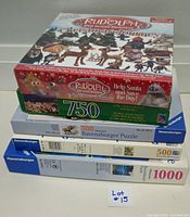 Stack of three Ravensburger puzzles and one sealed Rudolph board game on top