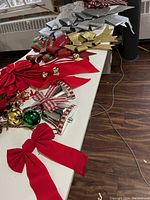 Large table display of numerous Christmas bows and festive decorations including large red fabric bows, glittery bows in gold, silver, and red, plus jingle bell ornaments.