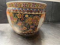 Front side of the planter pot showing floral and geometric painted decorations in gold, red, blue, and green on a black background panel.