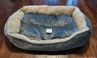 Front angle photo showing large blue corduroy-style textured dog bed with plush beige surround and removable cushion placed on wooden floor.