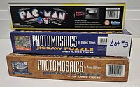 Side view of Pac-Man arcade game box placed atop three Photomosaics jigsaw puzzles boxes, showing branding and piece count for the puzzles.