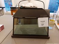 Brown metal and glass multi-candle holder, house-shaped with handle on top, visible on tabletop indoors.