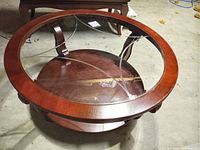 Top and angle view of a round coffee table with wooden frame and clear glass top with decorative segmented design, shown with dust on surface.