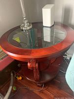 Front angle view of round wood and glass side table under lamp and electronic device.