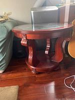 Side view of the round wood side table showing carved legs and curved supports with lower shelf.
