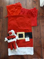 Santa-themed monkey plush toy and three Santa Claus gift bags laid out on wooden floor.