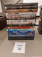 Photo shows a vertical stack of 15 DVDs including various movies and TV show titles such as The Rules of Attraction, Chicago, The Big Bang Theory Season 2, Shrek 2, Ice Age, and The Little Mermaid Special Edition.