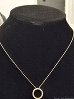 Full view of delicate 18-inch silver chain necklace with a circular pendant covered in diamond accents displayed on black jewelry display.