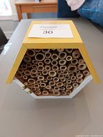 Front view of the small bee home showcasing tightly packed natural bamboo tubes inside a wooden house-shaped structure.