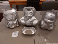 Photo showing three character-shaped aluminum cake pans for Garfield, Panda, and Carebear, along with a metal rack insert.