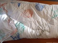 Close-up photo showing the shell and starfish motifs on the comforter fabric in pastel colors on white background.