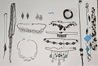 Overview of various pieces of costume jewelry laid out on a white surface including chains, necklaces, earrings pairs, and bracelets with various designs.
