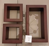 Three wooden shadow boxes arranged flat on a glass table, showing two smaller square boxes and one larger rectangular box, all with dark brown wooden frames and glass fronts.