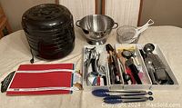 Entire lot including electric food dehydrator, stainless steel colander, kitchen utensils arranged in trays, and two colorful cutting pads