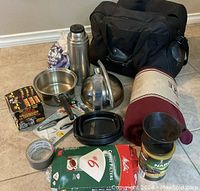 Emergency kit contents including thermos, metal cups, coffee filters, duct tape, and blanket alongside a black emergency bag