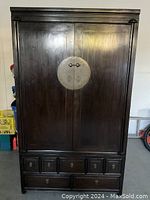 Front view of the closed dark wood armoire showing two large doors with circular metal hardware and five drawers below with metal pulls and keyholes.