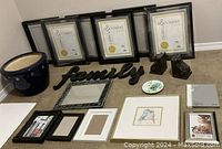 Photo showing six black floating frames, multiple assorted photo frames, a 'family' script decoration, framed bird print, budgie plate, blue ceramic plant pot, and one additional small frame or photo album.