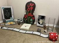 Overview photo showing all items in the lot arranged on carpeted floor including Swarovski crystal fish, violin painted with poppies, Venetian mask, metal shoe bookends, piggy bank, glass vase, framed sign, and salt and pepper shakers.
