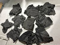 Overview of 12 black tactical security combat vests laid out on the ground, showing various styles and designs.