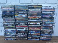 Photo of stacked DVDs showing wide variety of movie titles arranged in columns against white brick background.