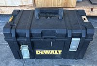 Front view of black DeWalt plastic tool box with metal latches and DeWalt logo on front.