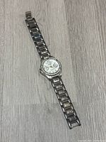 Full view of the DMQ watch lying flat, showing the linked metal band and round dial with rhinestone accents.