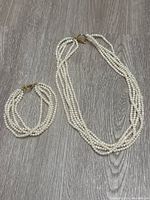 Full view of the freshwater pearl necklace and matching bracelet laid flat on a grey wood surface, showing multi-strand design and gold tone clasps.