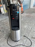 Stainless steel Glacier Bay water cooler unit standing on floor with power cord visible.