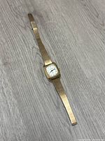 Full length image of the Bulova Accutron ladies wristwatch with gold tone strap laid flat on surface.