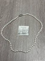 Full view of the Honora freshwater pearl necklace laid flat on a wood grain surface with accompanying Honora Pearls card