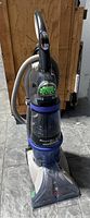 Full front view of Hoover Steam Vac Dual carpet cleaner showing upright design, water reservoir, hose at the back, and base with brush area.