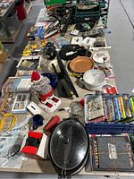 View of table with cookware, DVDs, electronics and various miscellaneous items seen from above.
