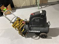 Side view of Husky air compressor showing wheels, handle, attached yellow air hose and motor housing.