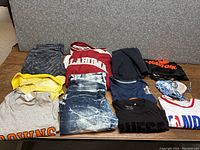 Top-down view of folded assorted clothing showing colors, logos, and styles including jeans, sweatshirts and sportswear.