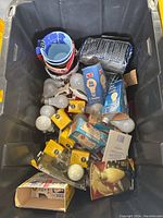 View of the tote filled with various lightbulbs mostly in packages, two ceramic mugs stacked inside each other, and some other household items including small framed art and charcoal bags.
